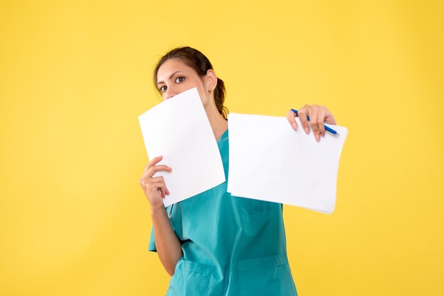 Giovane medico femminile di vista frontale in camicia medica con i documenti sullo scrittorio giallo