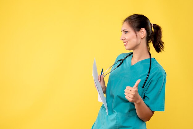 Giovane medico femminile di vista frontale in camicia medica con i documenti sullo scrittorio giallo