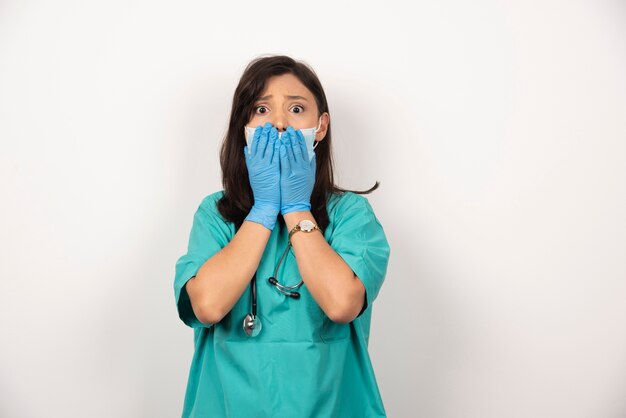 Giovane medico in maschera medica e guanti tenendo il viso su sfondo bianco.