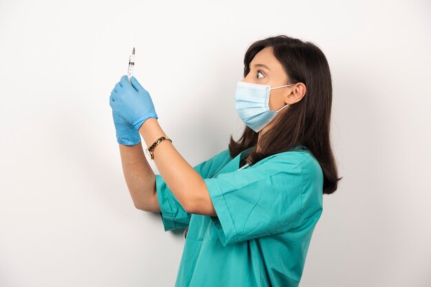 Giovane medico in maschera medica e guanti tenendo la siringa su sfondo bianco.