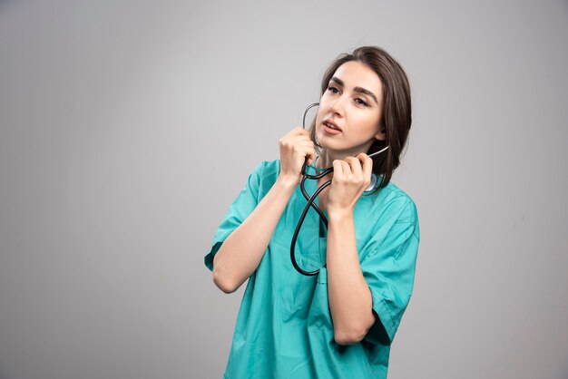 Giovane medico in uniforme utilizzando uno stetoscopio su sfondo grigio. Foto di alta qualità