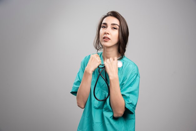 Giovane medico in uniforme utilizzando uno stetoscopio sul muro grigio.