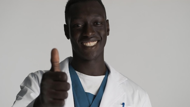 Giovane medico maschio afroamericano attraente che indica a te gesto sulla fotocamera che sembra felice su sfondo bianco