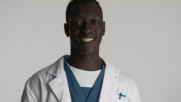 Giovane medico maschio afroamericano bello che sembra sorridente felice sulla macchina fotografica sopra priorità bassa bianca