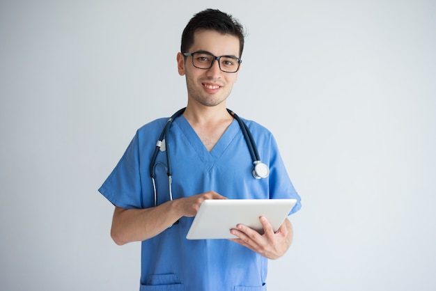 Giovane medico maschio astuto sorridente che per mezzo del calcolatore del ridurre in pani.