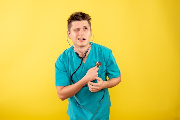 Giovane medico maschio di vista frontale in vestito medico con lo stetoscopio su priorità bassa gialla