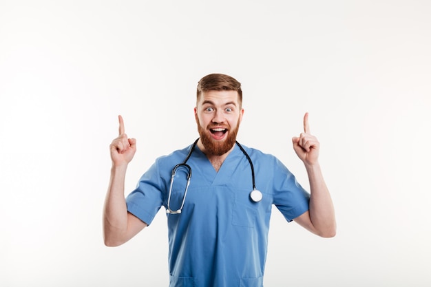 Giovane medico maschio emozionante che indica due dita su al copyspace