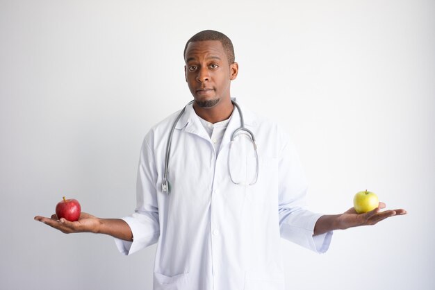 Giovane medico maschio nero serio che tiene le mele verdi e rosse.