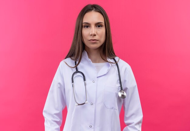 giovane medico ragazza indossa stetoscopio abito medico sulla parete rosa isolata