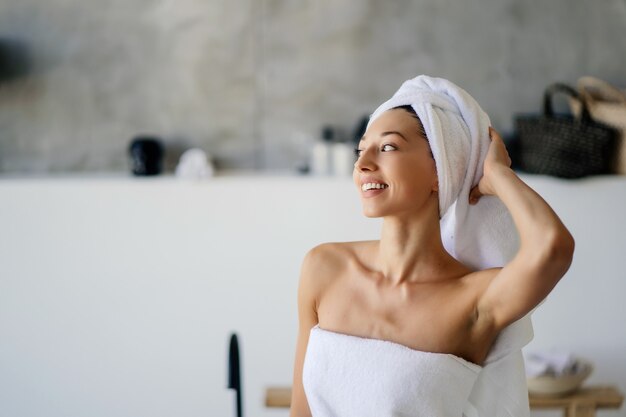 Giovane modella caucasica rilassata con un asciugamano bianco, si sente rinfrescata dopo aver fatto la doccia, ha una pelle morbida e pulita, posa in un bagno accogliente. Donne, bellezza e concetto di igiene.