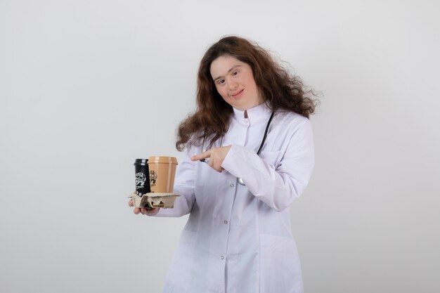 giovane modella in uniforme bianca che punta a un cartone con tazze di caffè.