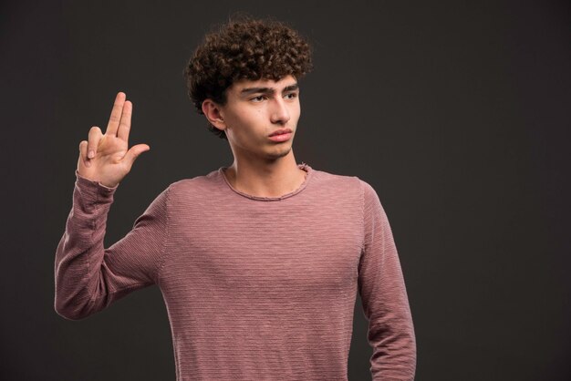 Giovane modello con i capelli ricci che fanno il segno della pistola.