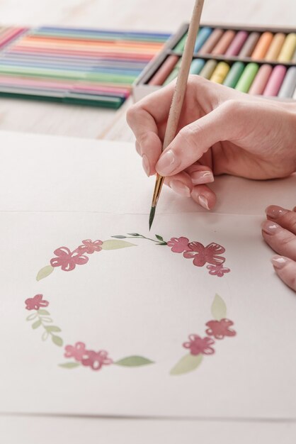 Giovane modello di fiori del disegno dell'artista con la pittura e la spazzola dell'acquerello nel luogo di lavoro