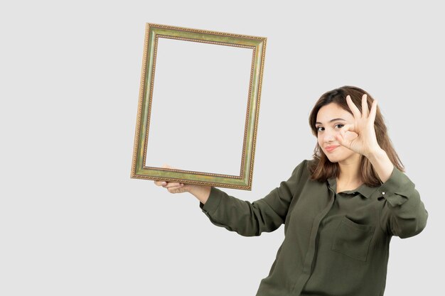 Giovane modello femminile adorabile che tiene cornice di legno vuota. Foto di alta qualità