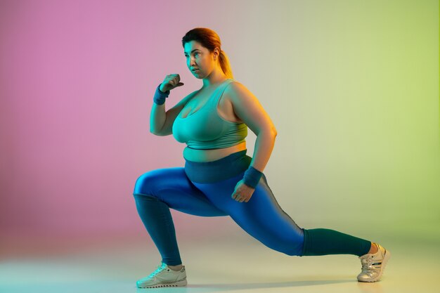 Giovane modello femminile caucasico plus size allenamento su parete verde viola sfumata