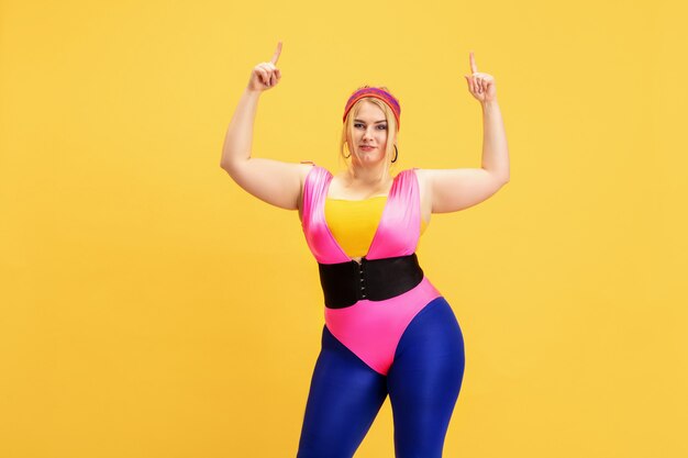 Giovane modello femminile caucasico plus size che si allena su giallo