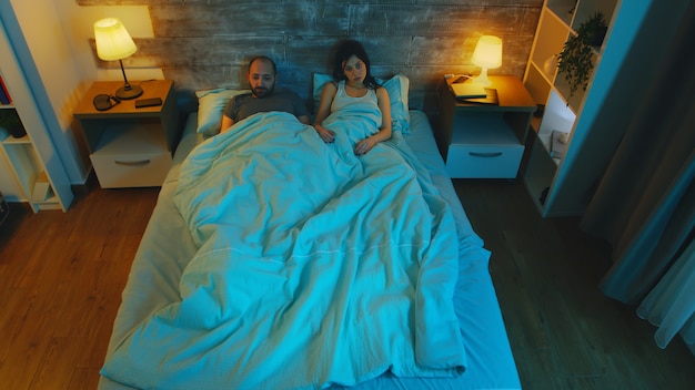 Giovane moglie con il marito sotto le lenzuola che gli dice che vuole il divorzio. Luce di luna blu nella stanza.