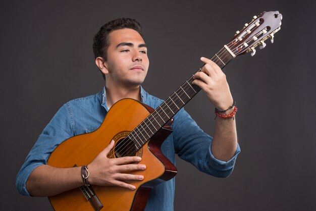 Giovane musicista che tiene chitarra su sfondo nero