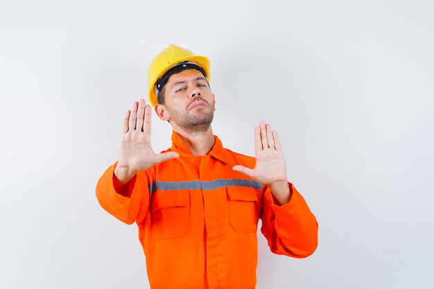 Giovane operaio che mostra il gesto di rifiuto in uniforme, casco.