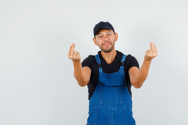 Giovane operaio in uniforme che gesturing con le dita e che sembra mite, vista frontale.