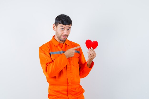 Giovane operaio in uniforme che punta al cuore rosso e che sembra positivo.