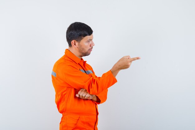 Giovane operaio in uniforme che punta davanti a lui e che sembra serio.