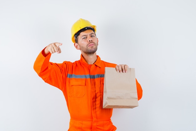 Giovane operaio in uniforme che tiene il sacchetto di carta, indicando davanti.