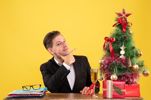 Giovane operaio maschio di vista frontale che si siede con i regali di natale e l'albero