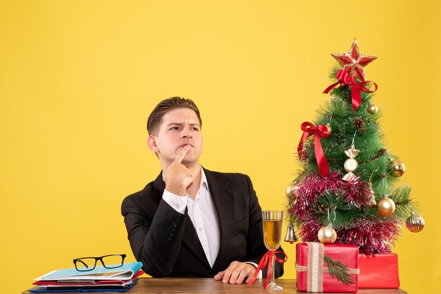 Giovane operaio maschio di vista frontale che si siede con i regali di natale e l'albero