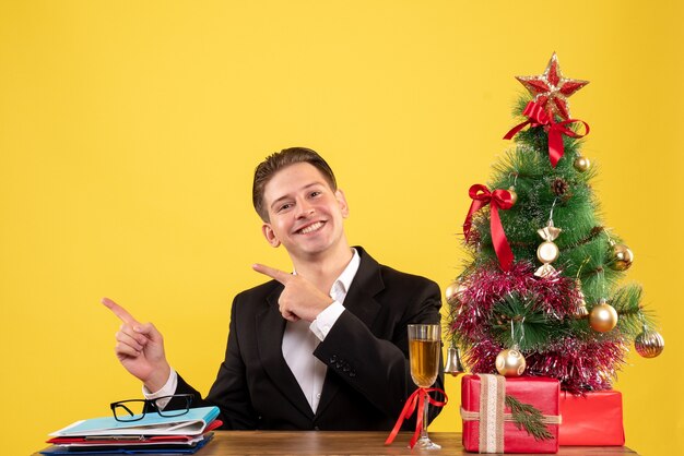 Giovane operaio maschio di vista frontale che si siede con i regali di natale e l'albero