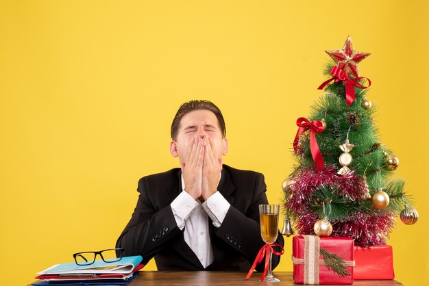 Giovane operaio maschio di vista frontale che si siede con i regali di natale e l'albero