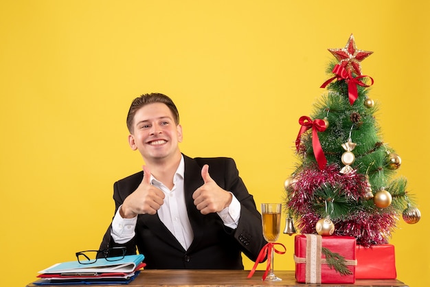 Giovane operaio maschio di vista frontale che si siede con i regali di natale e l'albero