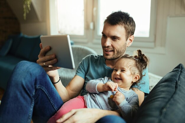 Giovane padre e figlia felici che si divertono mentre prendono selfie con la tavoletta digitale a casa