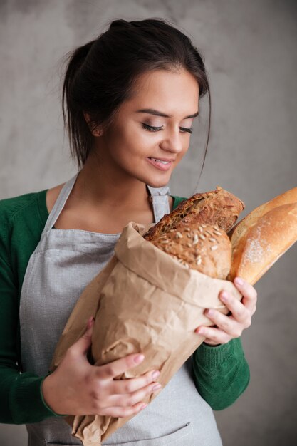 Giovane panettiere felice della signora che sta e che tiene pane.