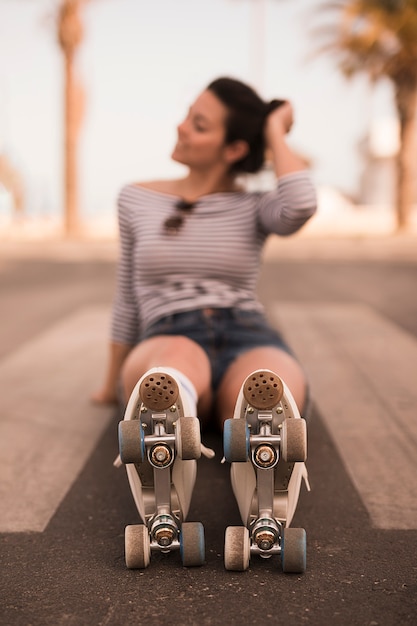 Giovane pattinatore femminile Defocused che si siede sulla strada con il pattino del rullo in sue gambe