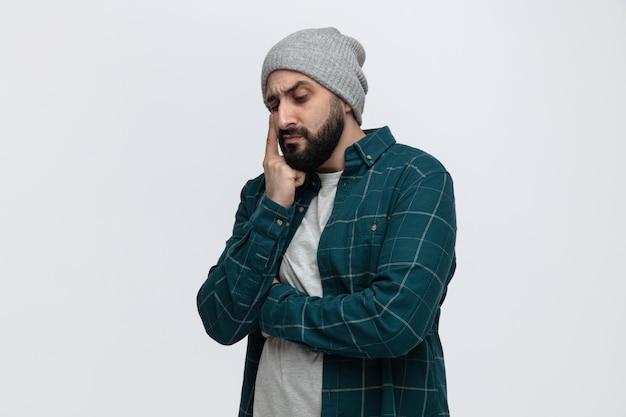 Giovane premuroso che indossa il cappello invernale tenendo la mano sul mento guardando in basso isolato su sfondo bianco