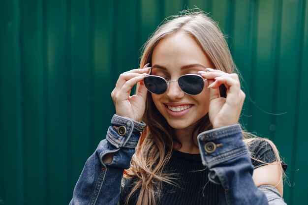 Giovane ragazza abbastanza attraente in vestiti di jeans in bicchieri su un semplice sfondo verde scuro con un posto vuoto per il testo