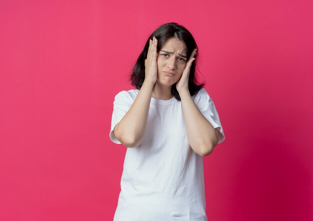 Giovane ragazza abbastanza caucasica dispiaciuta che mette le mani sul viso che guarda l'obbiettivo isolato su priorità bassa cremisi con lo spazio della copia