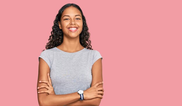 Giovane ragazza afroamericana che indossa abiti casual faccia felice sorridente con le braccia incrociate guardando la fotocamera persona positiva