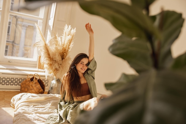 Giovane ragazza allegra dalla carnagione chiara che sorride guardando la fotocamera mentre è seduto sul pavimento in una stanza confortevole La donna bruna con i capelli lunghi indossa abiti casual Concetto di riposo e recupero