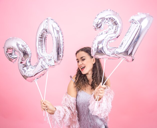 Giovane ragazza allegra in abito festivo su sfondo rosa studio in posa tenendo palloncini d'argento per il concetto di nuovo anno