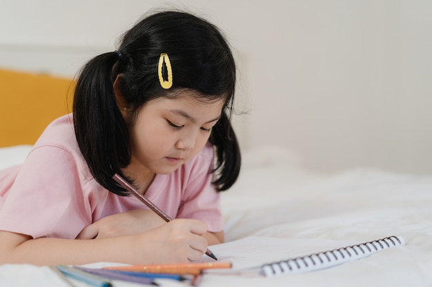 Giovane ragazza asiatica che disegna a casa. Il bambino giapponese del bambino della donna dell'Asia si rilassa il fumetto felice di tiraggio di divertimento di resto in sketchbook prima di dormire la menzogne sul letto, ritiene la comodità e la calma in camera da letto al concetto di notte.