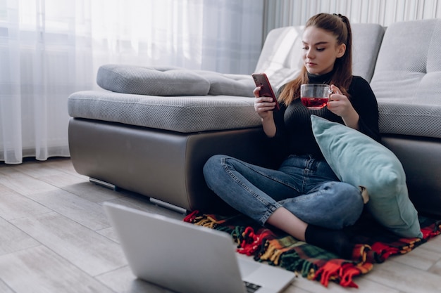 Giovane ragazza attraente a casa che lavora con un computer portatile e che parla al telefono. comfort e intimità a casa. home office e lavoro da casa. lavoro online a distanza.