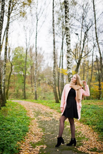 Giovane ragazza bionda al cappotto rosa posato sul parco autunnale