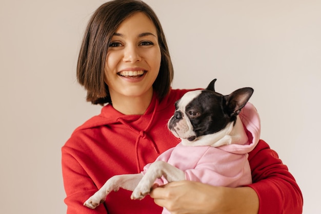 Giovane ragazza bruna caucasica allegra con il suo cane indossa la felpa con cappuccio insieme su sfondo bianco Concetto di cura del cane