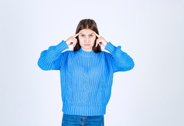 Giovane ragazza bruna in maglione blu in attesa con espressione seria.