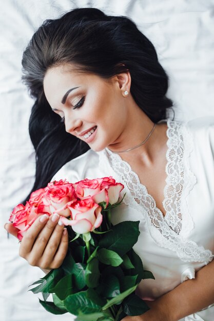 giovane ragazza bruna si sdraia sul suo letto, al mattino e tiene in mano un Belle rose. Vista dall'alto.