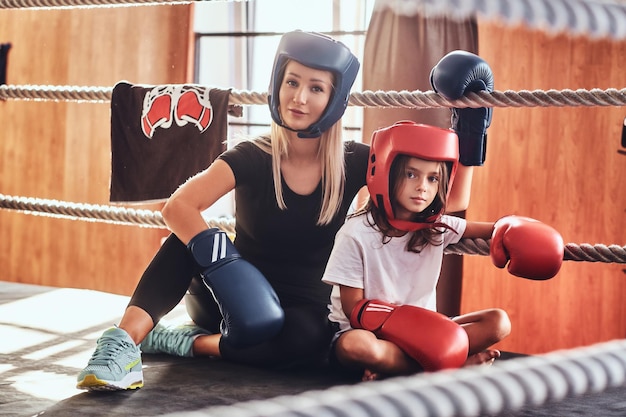 Giovane ragazza carina con il casco e il suo bellissimo allenatore di boxe femminile stanno posando per il fotografo sul ring.