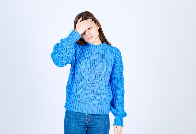 Giovane ragazza castana in maglione blu che ha emicrania su bianco.