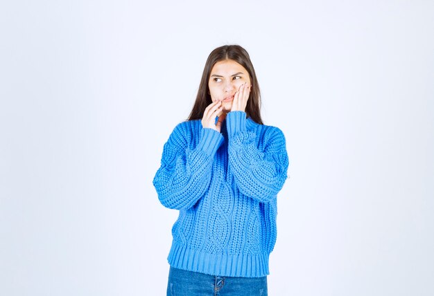 Giovane ragazza castana in maglione blu che ha mal di denti su bianco.